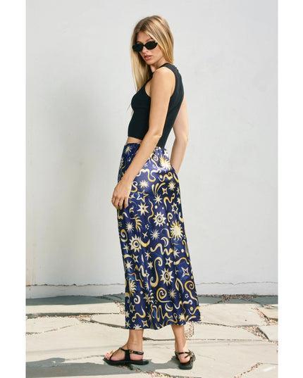 Woman wearing a black top and a long, patterned skirt against a white wall.