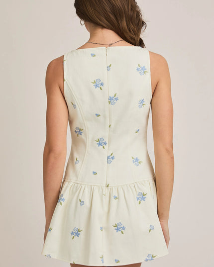 Woman wearing a light-colored dress with floral embroidery on a plain background