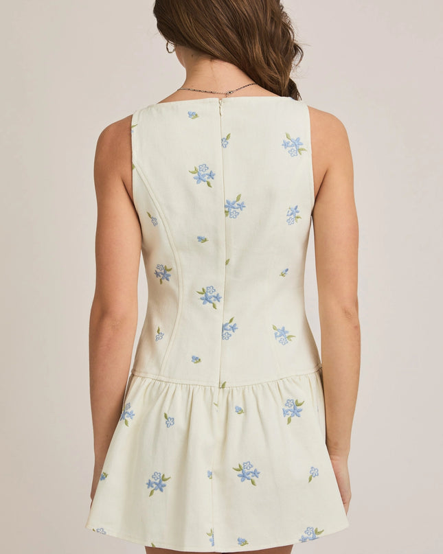 Woman wearing a light-colored dress with floral embroidery on a plain background