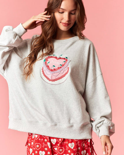 Woman wearing a light gray sweatshirt with a heart design on a pink background