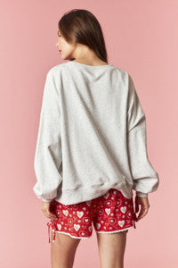 Person wearing a light gray sweatshirt and red shorts with heart patterns on a pink background