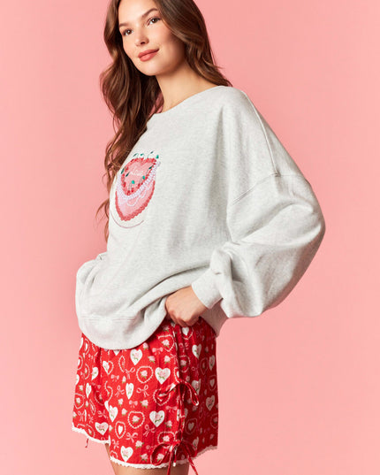 Woman wearing a white oversized sweater with a watermelon design and red shorts with heart patterns on a pink background