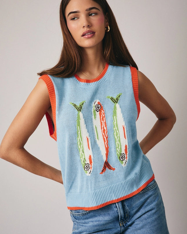 Woman wearing a light blue sleeveless sweater with fish designs on a plain background