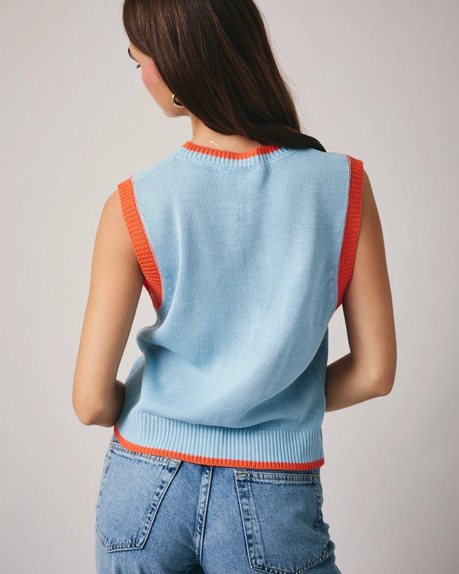 Woman wearing a light blue sleeveless sweater with red trim on a plain background