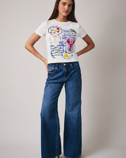 Woman wearing a white t-shirt with colorful graphics and blue jeans on a plain background