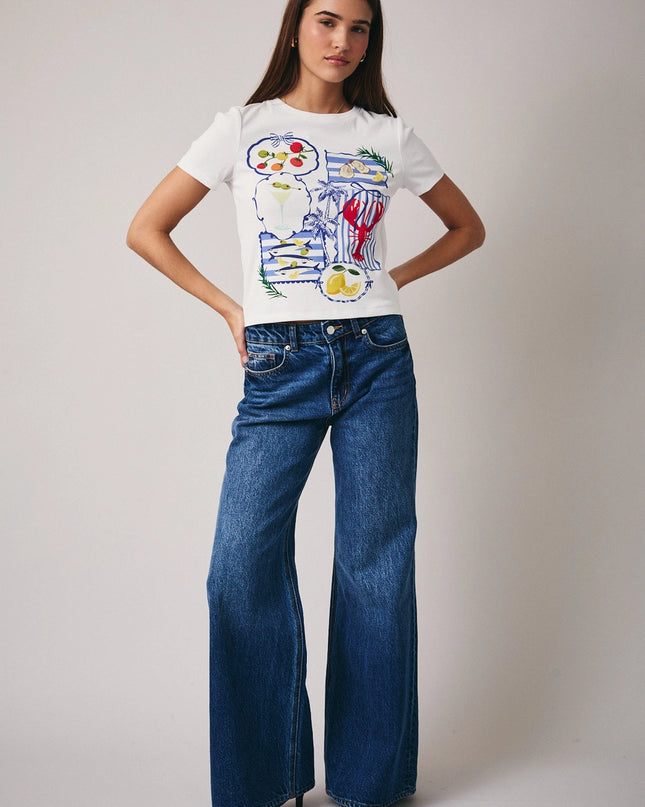 Woman wearing a white t-shirt with colorful graphics and blue jeans on a plain background
