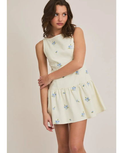 Woman wearing a light yellow dress with floral patterns on a plain background