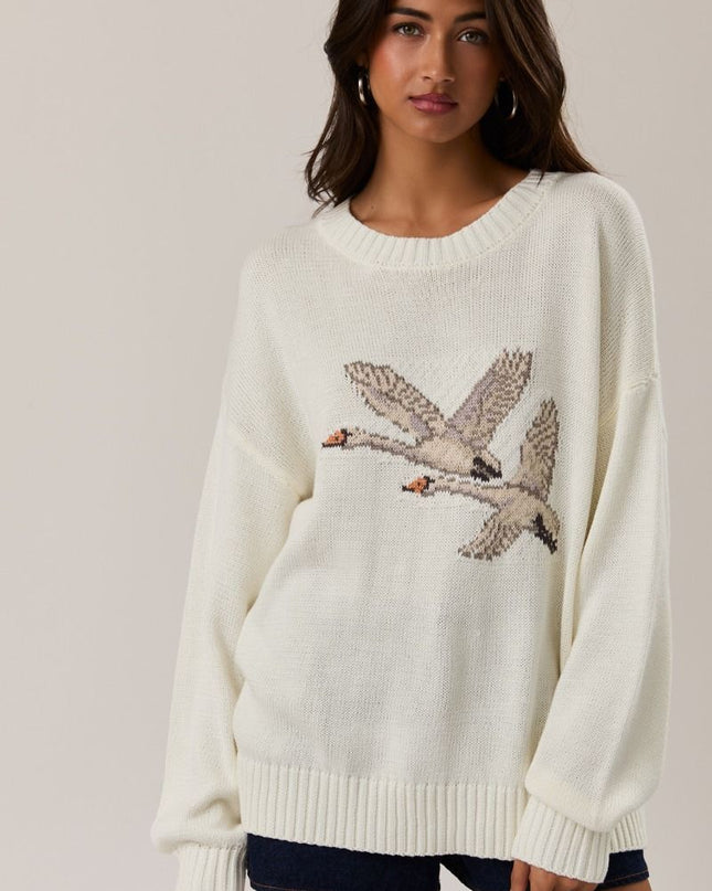 Woman wearing a cream sweater with swan design on a plain background