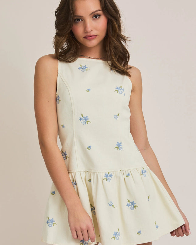 Woman wearing a light-colored dress with floral embroidery on a plain background