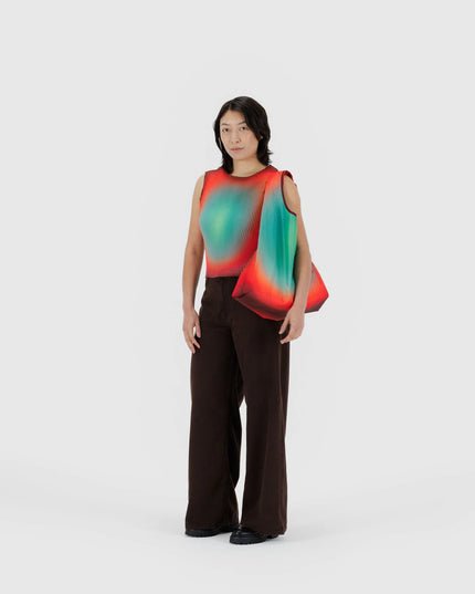 Person wearing a sleeveless, multicolored top with a plain background