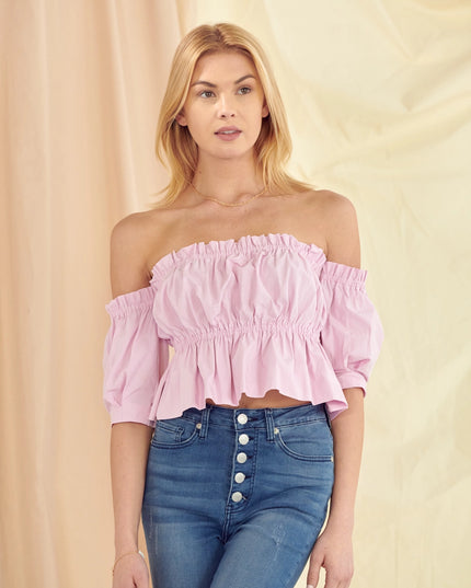 Woman wearing a pink off-shoulder top and blue jeans against a beige background