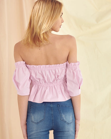 Woman wearing a pink off-shoulder top and blue jeans against a beige background