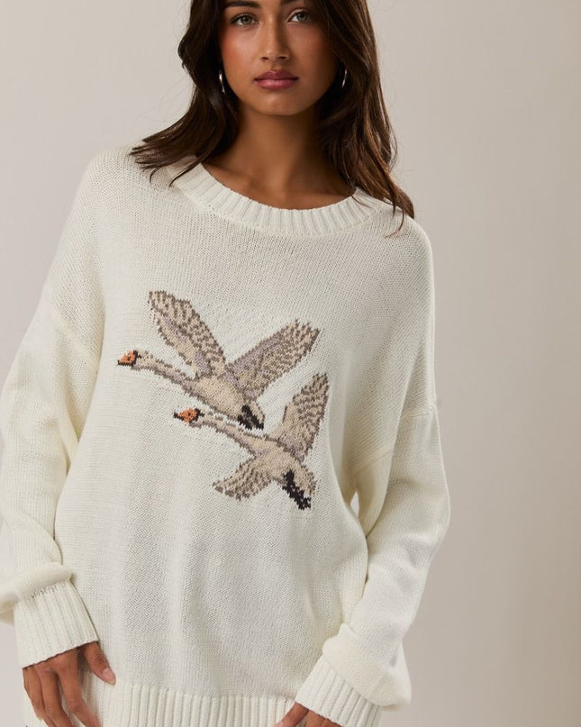 Woman wearing a white sweater with bird design against a plain background