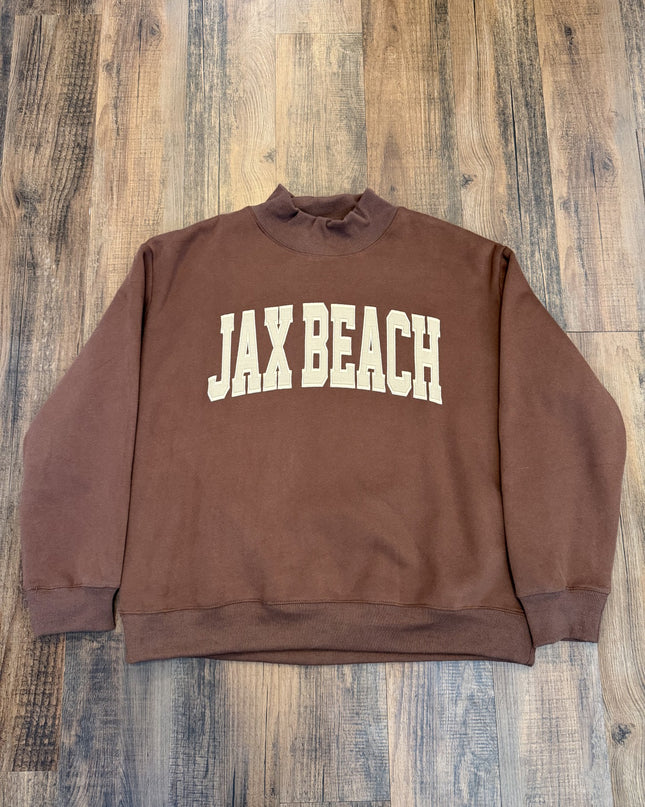 Brown sweatshirt with 'JAX BEACH' text on a wooden surface