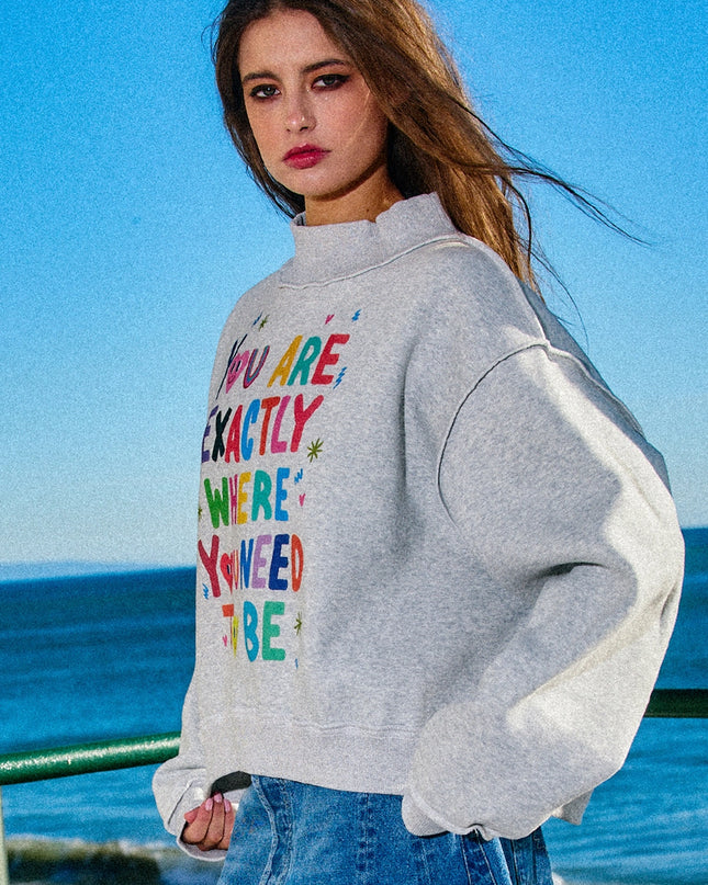 Woman wearing a gray hoodie with colorful text by the ocean