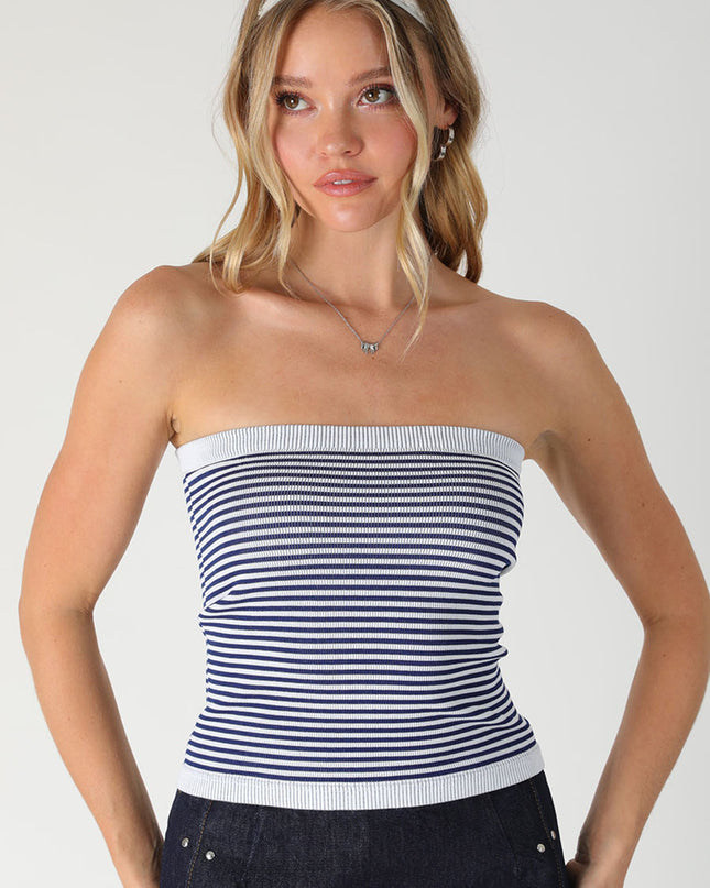 Woman wearing a striped tube top and dark pants on a plain background