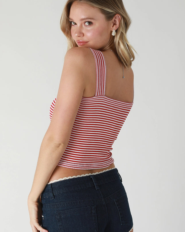 Woman wearing a red and white striped tank top and dark denim shorts on a plain background