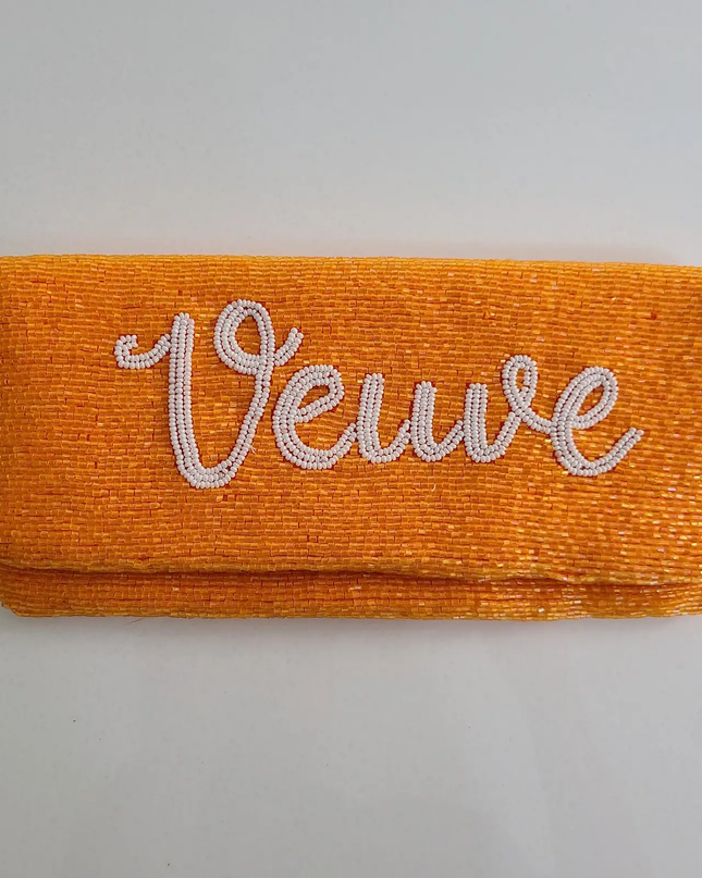 Orangish-yellow clutch beaded all over with white script that says "Veuve in cursive"